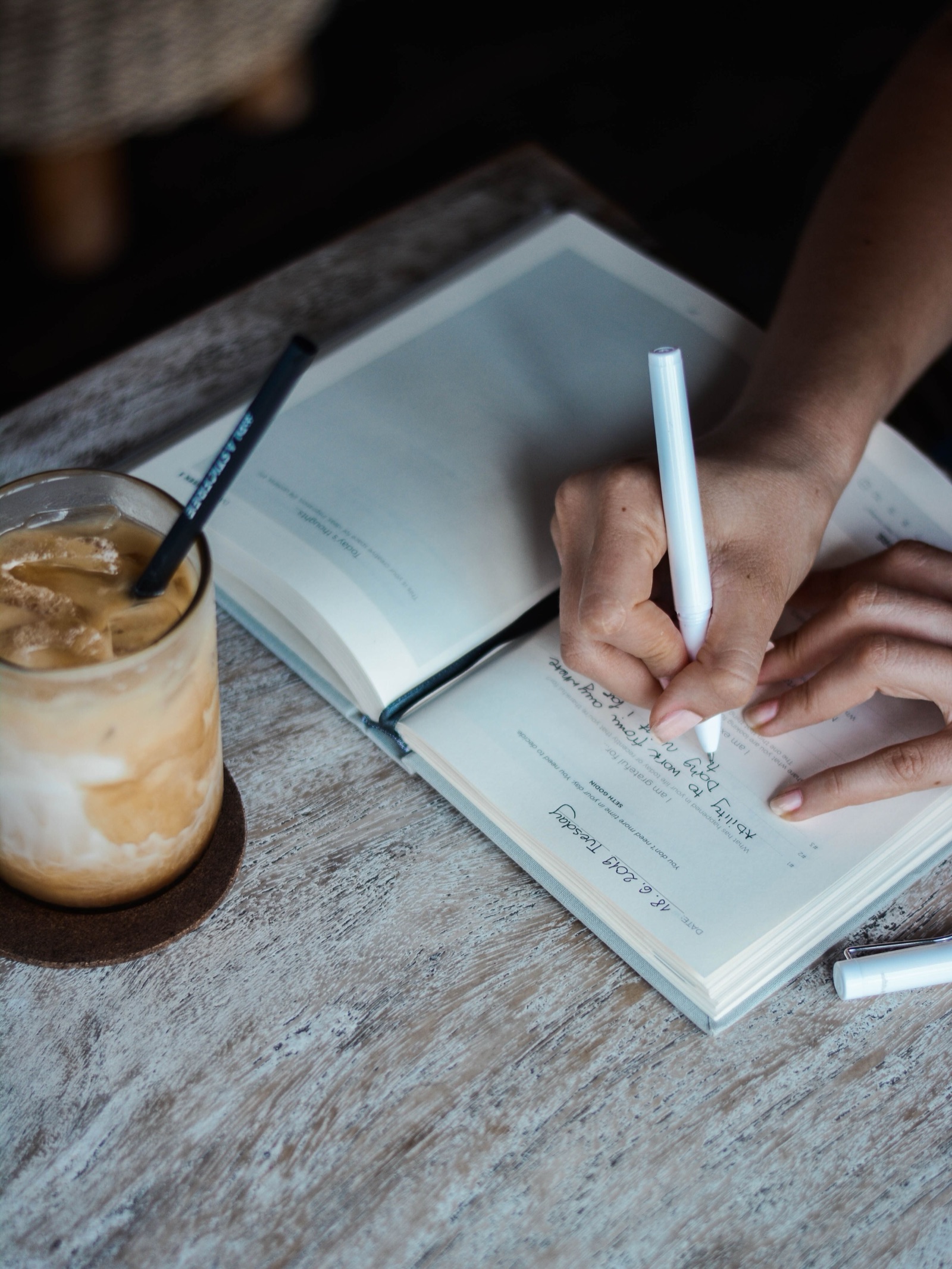 Person writing in a gratitude journal beside an iced coffee