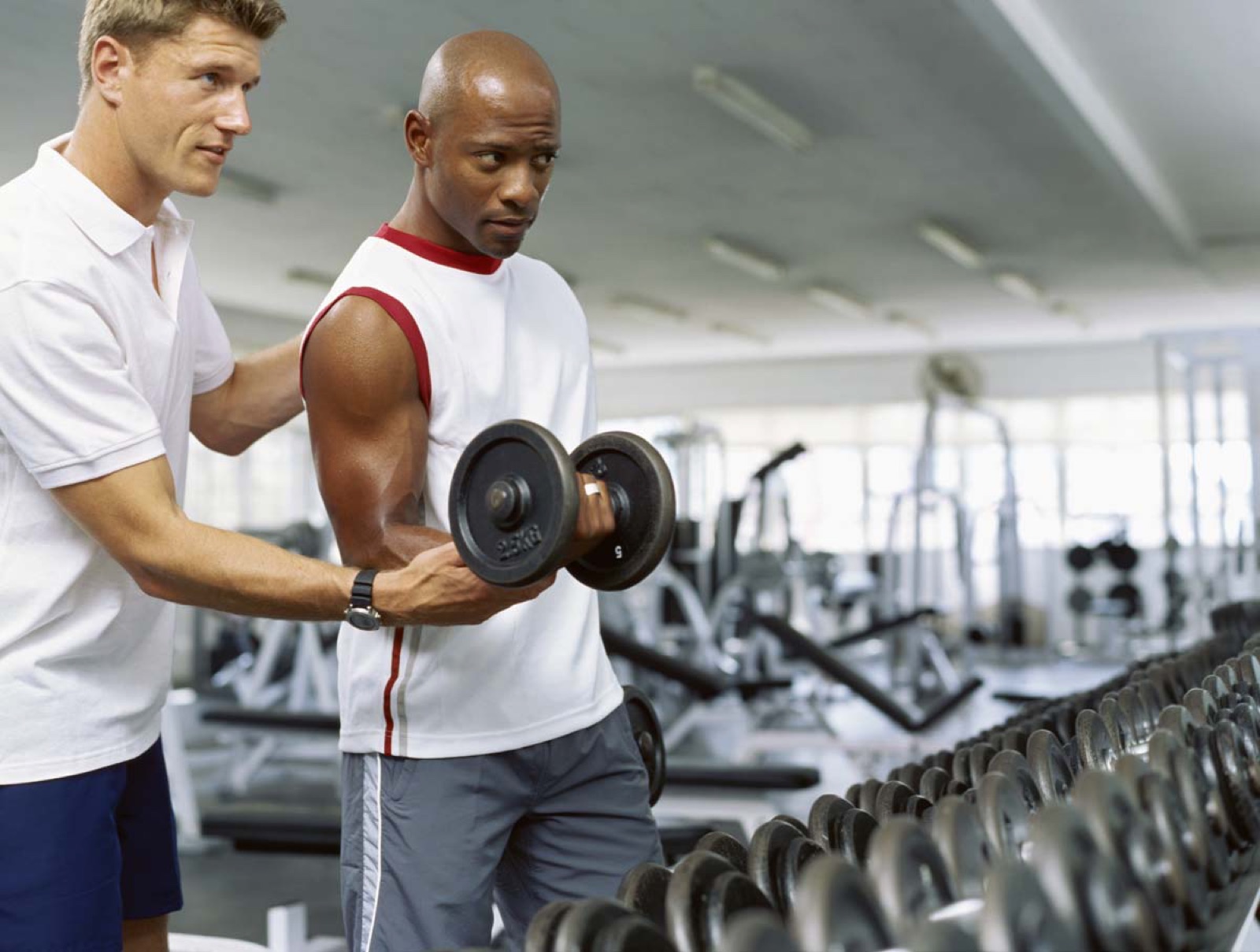 Personal trainer helping a man curl a dumbbell in a gym