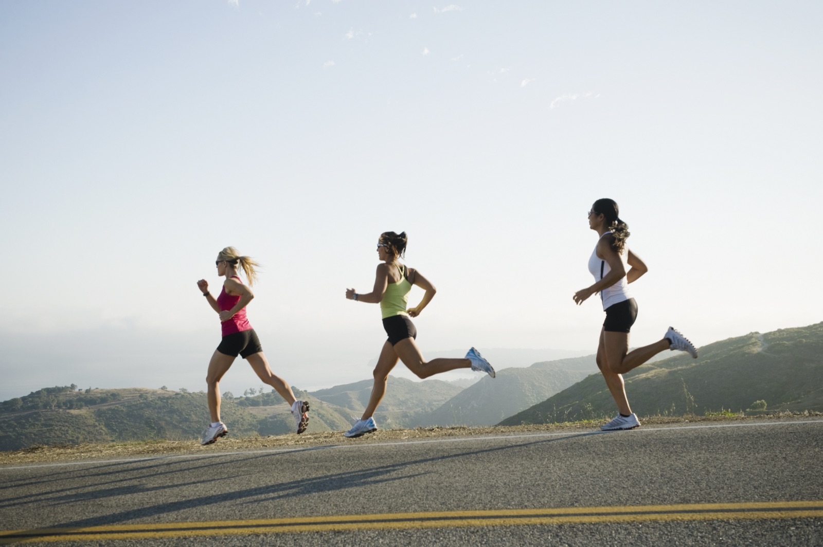 Three women jogging along a road through rolling hills